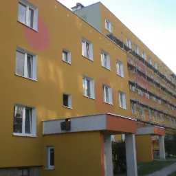 Ocieplony budynek wielorodzinny z pomarańczowymi akcentami i rusztowaniami na części elewacji.